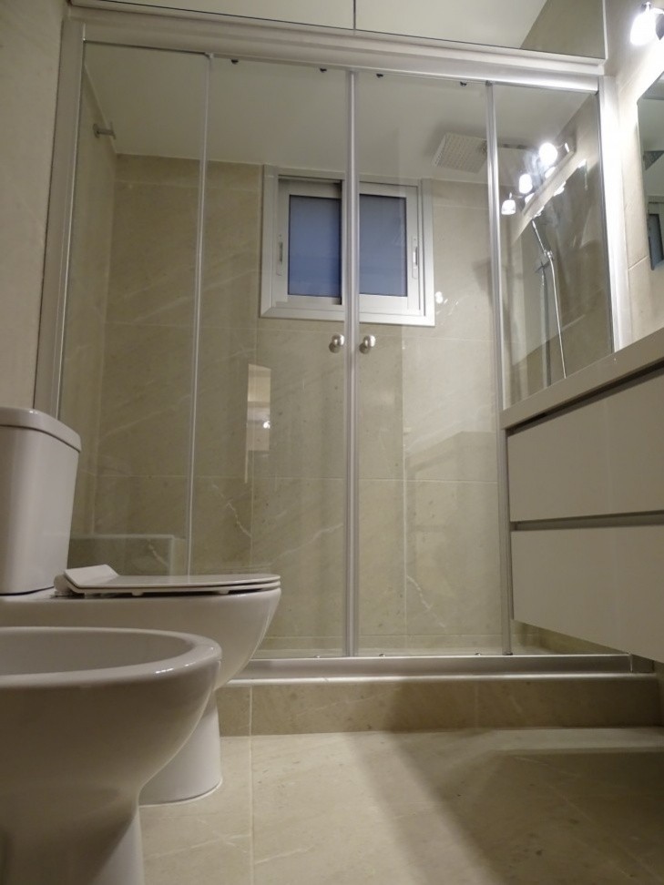 Picture of the main toilet room of the apartment having a large shower unit, a sink cabinet, a toilet unit, a bidet unit, and a mirror.