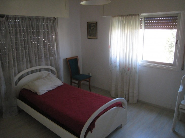 One of the rooms of the flat with a single bed frame, a sing mattress, a two windows