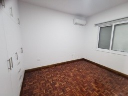 Picture of the second bedroom, having large cupboards, one a/c unit, window, and laminated parquet flooring.