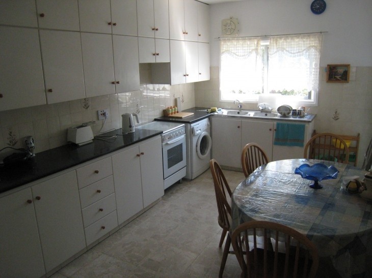 The space of the kitchen, with a dining table with six chairs, a stove, an oven, a washing machine, and counters