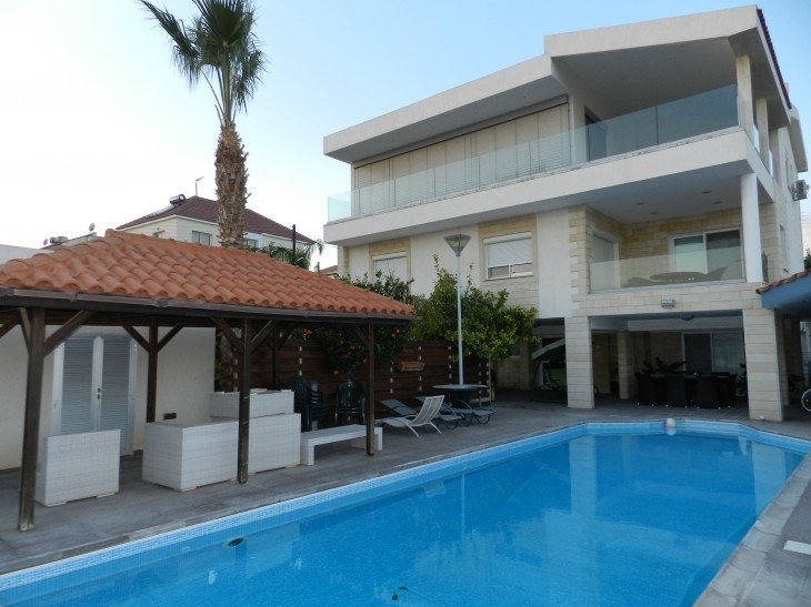 the exterior area of the house that has a private swimming pool, a pavilion, outdoor table and chairs of white color and sunbeds