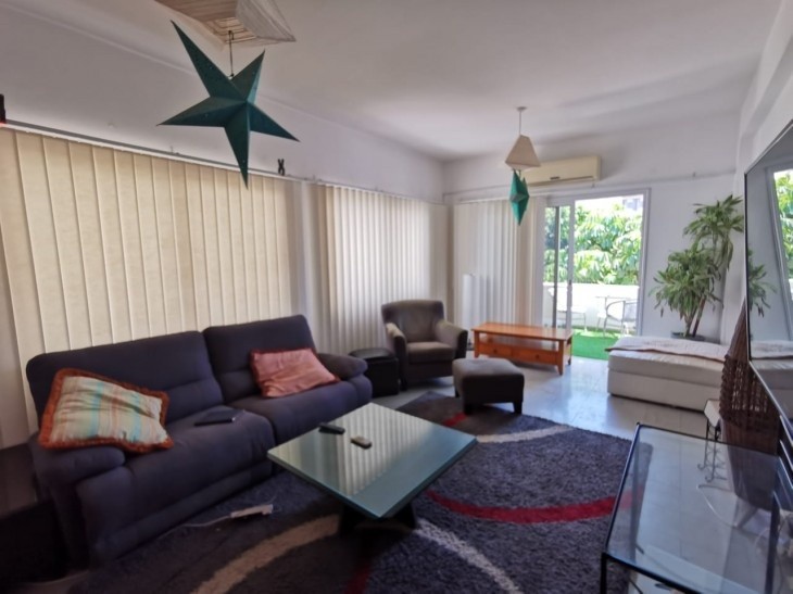 the space of the living room area that has a big carpet, coffee table, another glass coffee table, two seated sofa, armchair, stool, a/c units and balcony doors